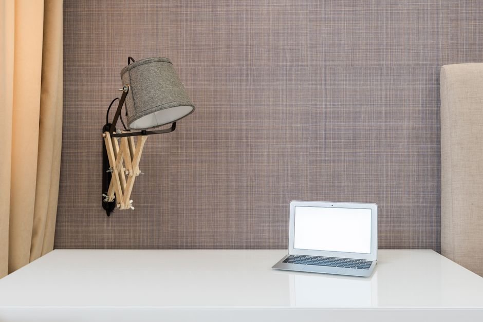 Interior of workplace with opened netbook on white table near wall with lamp