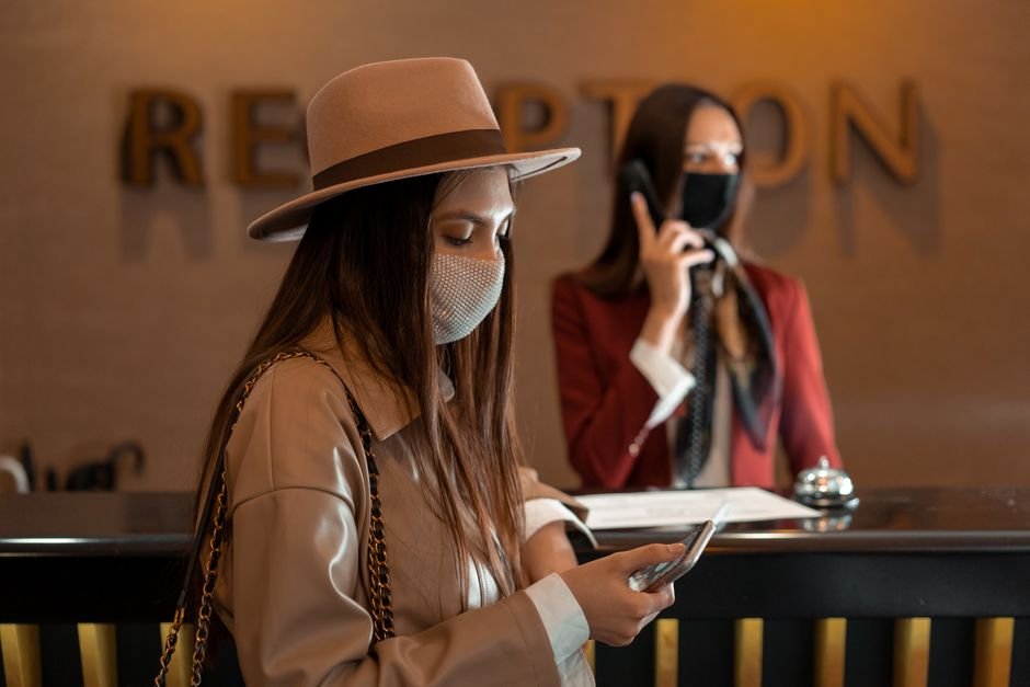 Woman wearing a mask checking her phone at a hotel reception during COVID-19.